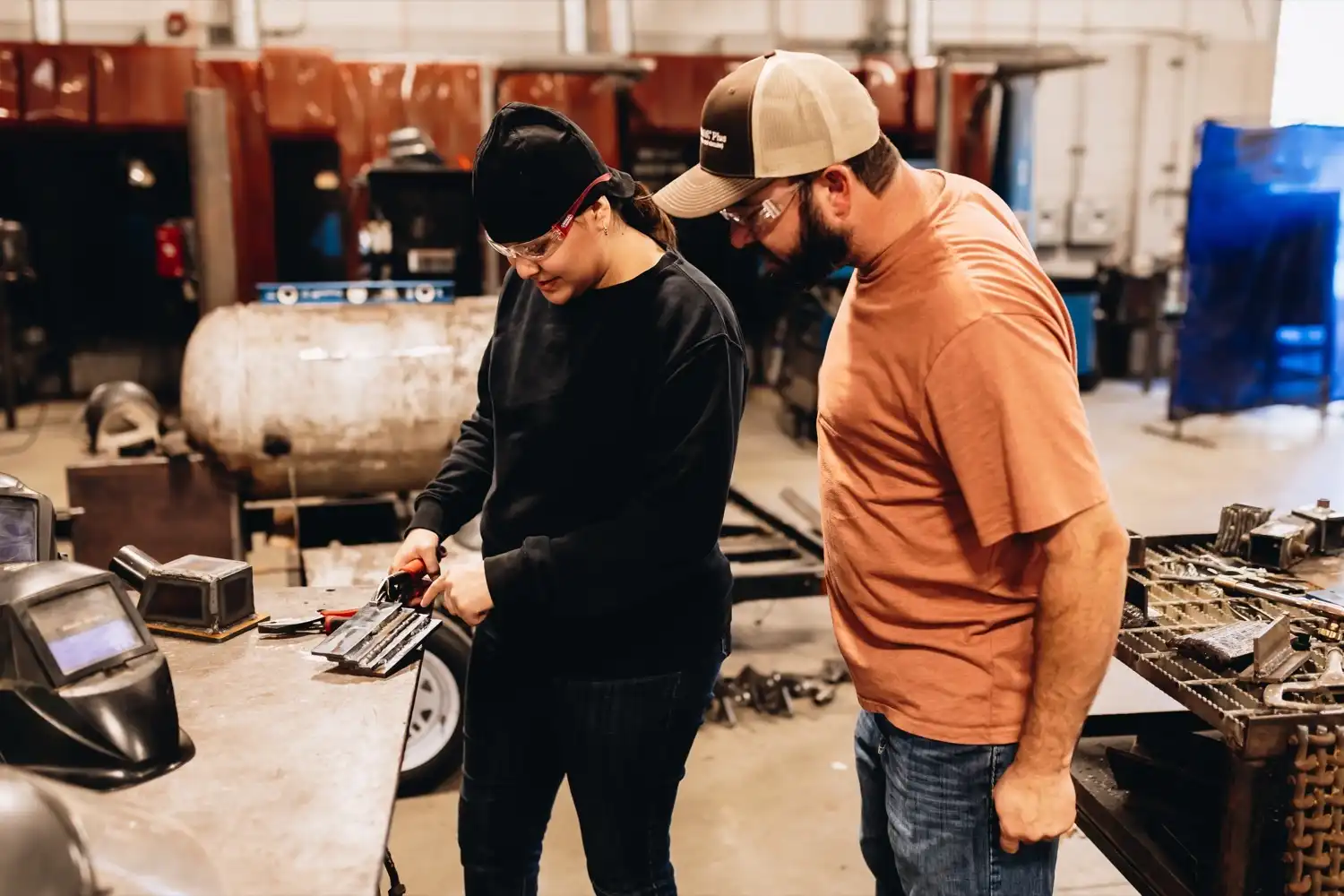 A welding instructor observes a student examining a metal weld in the welding lab.