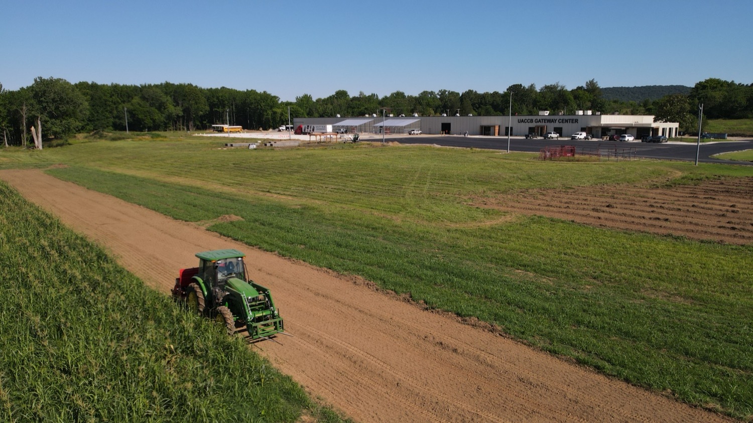 A tractor pulls planting equipment through a field with the UACCB Gateway Center visible in the background.