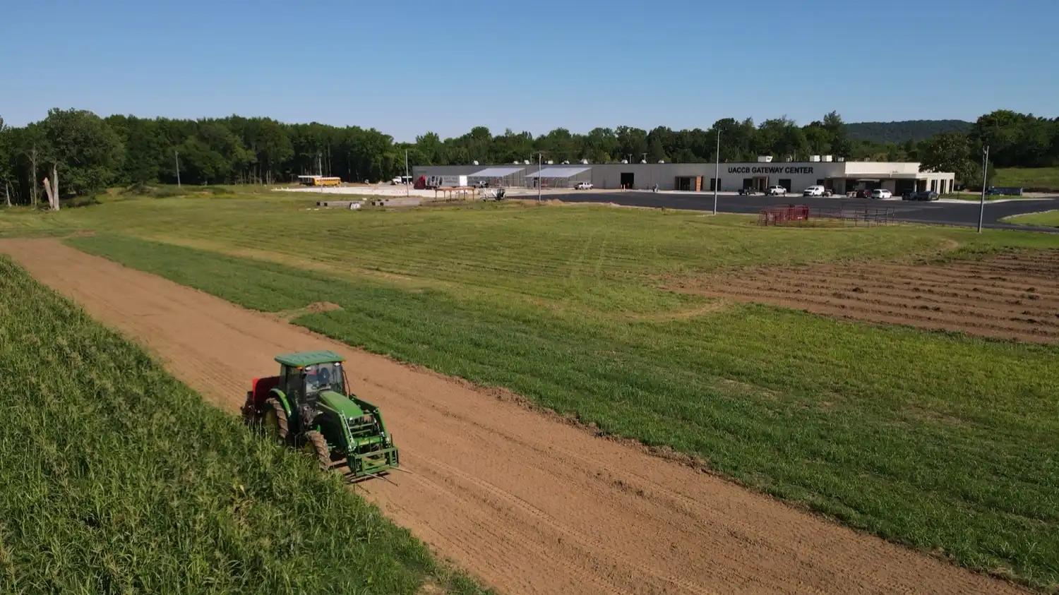 An aerial view shows a tractor working along the edge of a field near the UACCB Gateway Center.