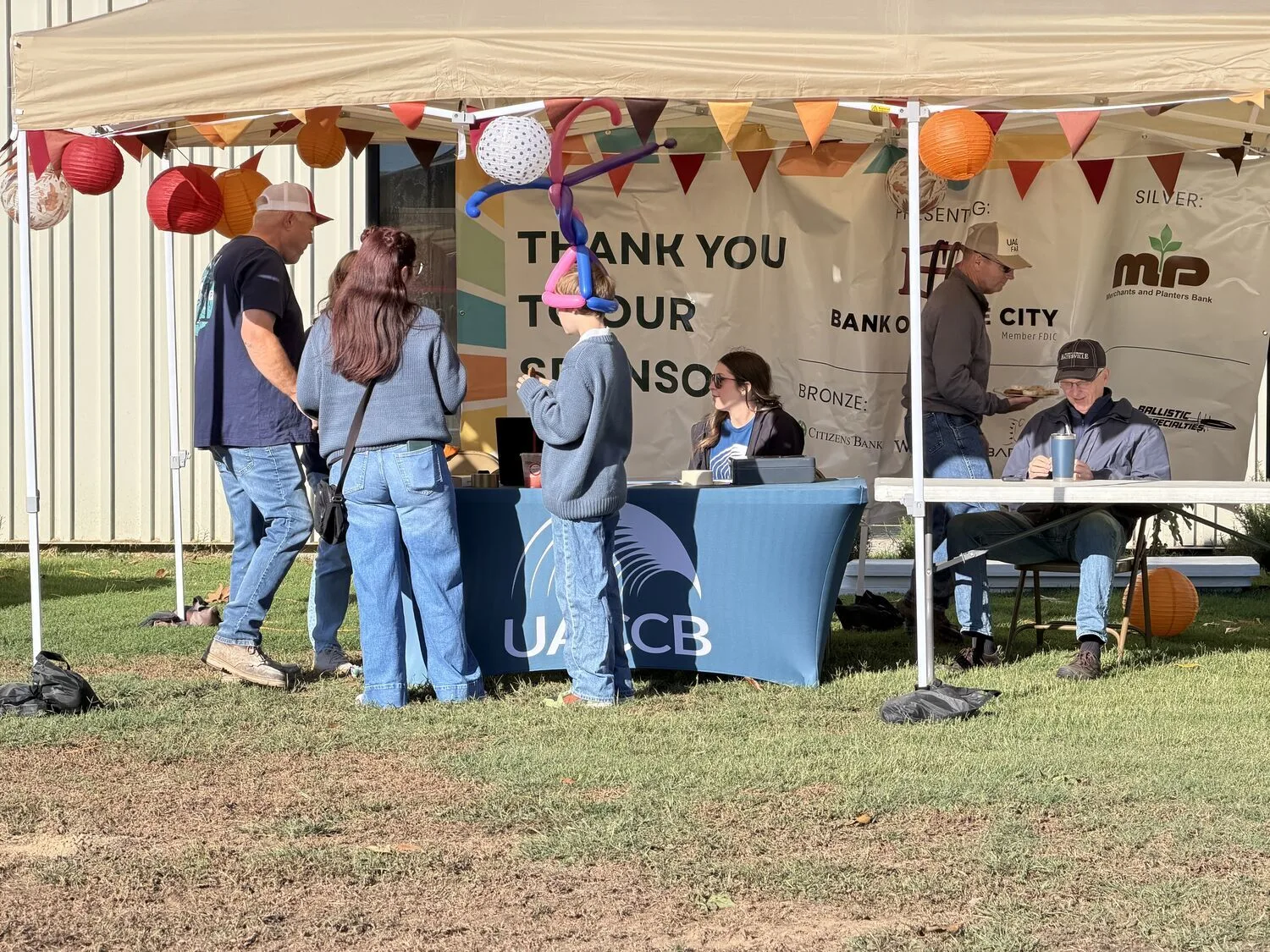 Visitors gather at a UACCB booth decorated with fall lanterns and bunting.